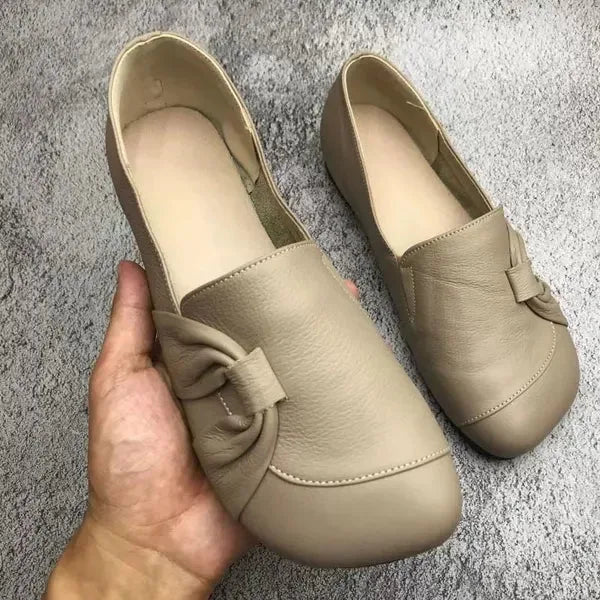 Beige leather flat with soft knot trim and matching insole shown resting on a grey textured surface