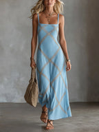 Light blue sleeveless maxi dress with crisscross tan embroidery, worn with strappy sandals and a woven bag