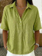 Green linen-look blouse with open collar and button placket, shown on a model with layered necklaces
