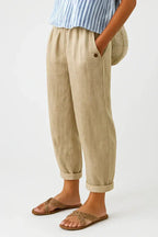 Side view of beige linen-blend cropped trousers with elastic waist, button pocket detail, worn with raffia slide sandals
