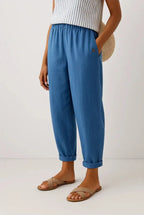 Mid blue cropped trousers in soft woven fabric, elastic waistband and button pocket, styled with tan slide sandals