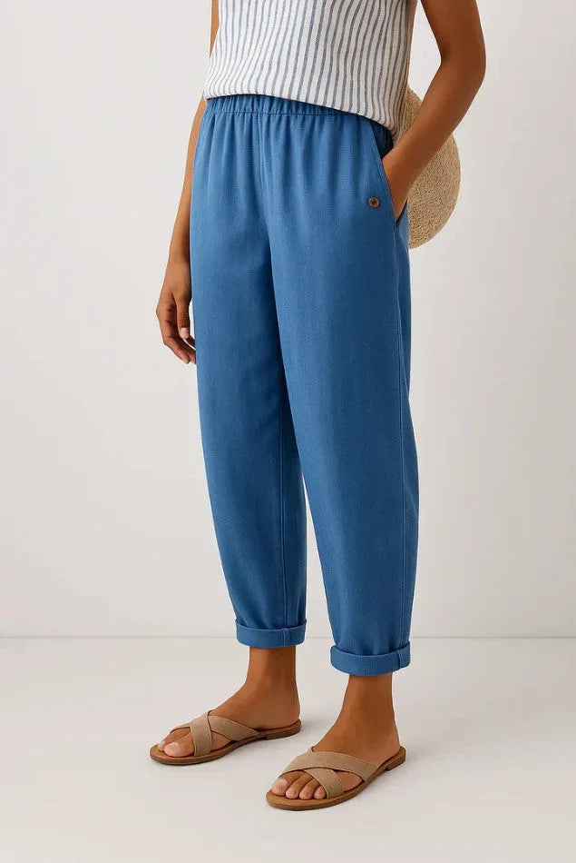 Mid blue cropped trousers in soft woven fabric, elastic waistband and button pocket, styled with tan slide sandals