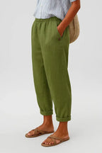 Olive green cropped trousers with rolled cuffs, relaxed tapered leg and hand resting in side pocket