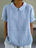 Close-up front view of a light blue linen-look blouse with a Peter Pan collar and short puff sleeves