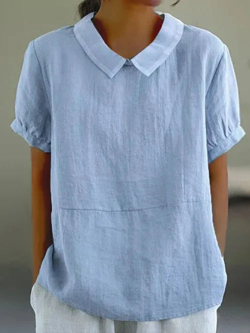 Close-up front view of a light blue linen-look blouse with a Peter Pan collar and short puff sleeves