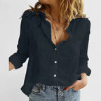 Close-up of a woman wearing a navy linen button-down shirt with a soft wavy lapel collar and delicate layered necklaces