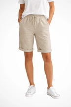 Front view of beige linen-look shorts with elastic drawstring waist and cuffed hems, styled with white t-shirt and sneakers