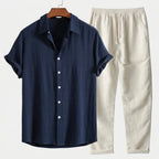Navy blue linen short-sleeve button-up shirt matched with cream linen drawstring pants, hung against a plain background