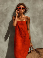 Close-up of the square neckline and thin straps of the orange linen maxi dress, paired with red sunglasses and tousled hair