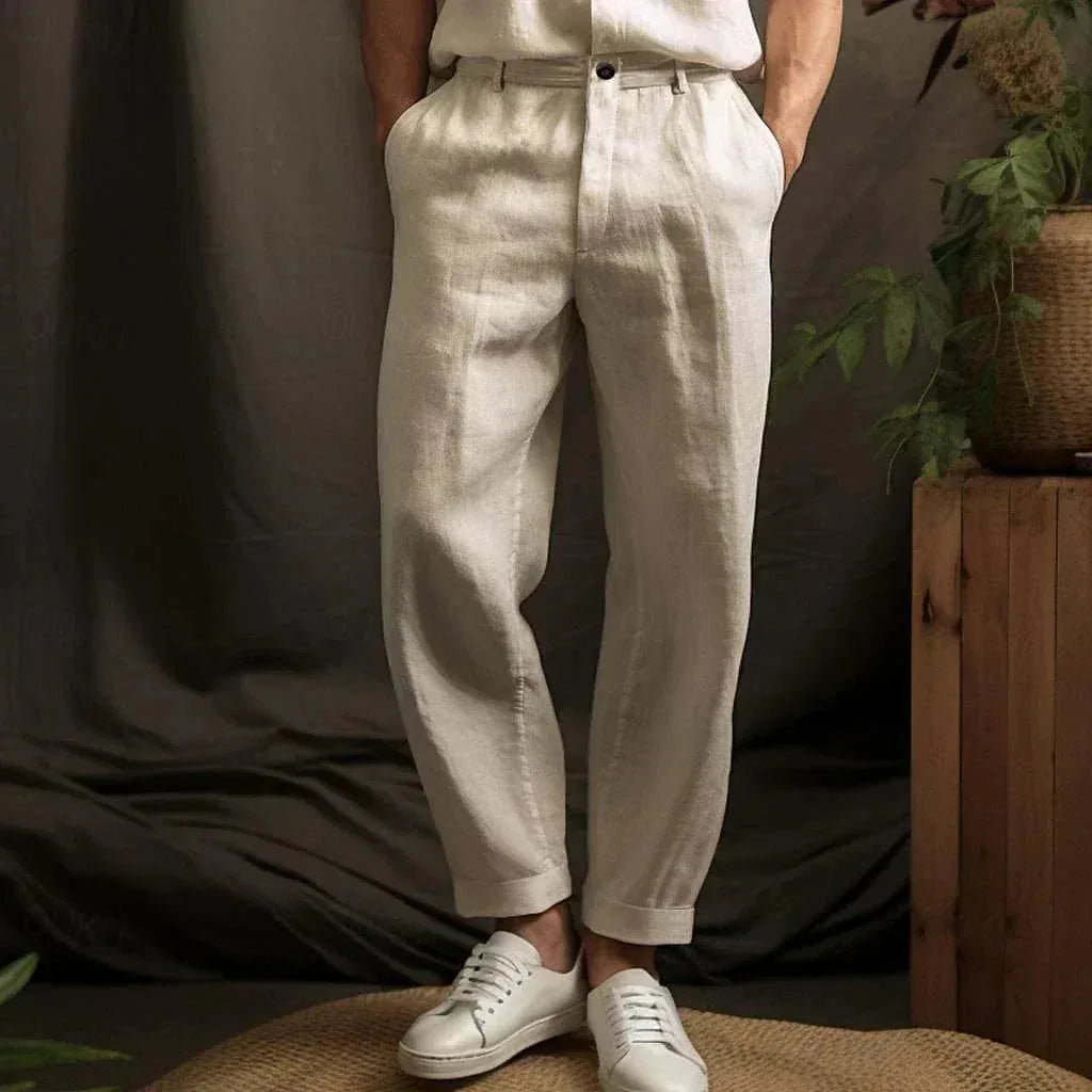 Front view of beige linen tapered trousers with cuffed hems, styled with a matching linen shirt and white sneakers.
