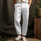 Close-up front view of white linen tapered pants with a cuffed hem, paired with a linen shirt and white sneakers.