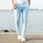 Man wearing light blue linen pants from behind, standing on a waterside path with drawstring waist visible