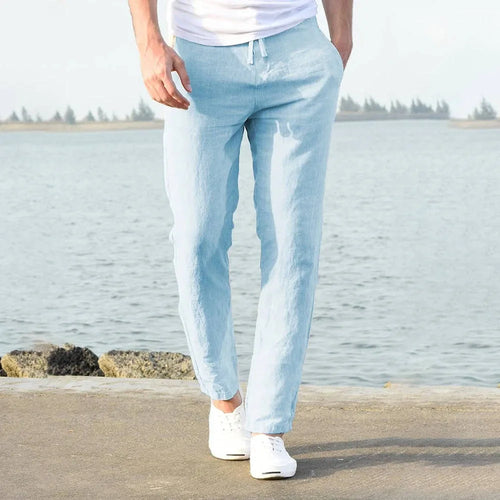 Man wearing light blue linen pants from behind, standing on a waterside path with drawstring waist visible