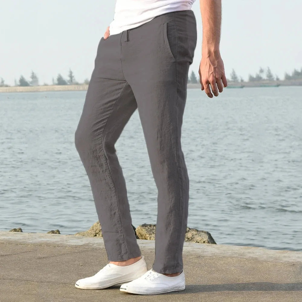 Man in light khaki linen pants seen from behind with white t-shirt and sneakers by the water
