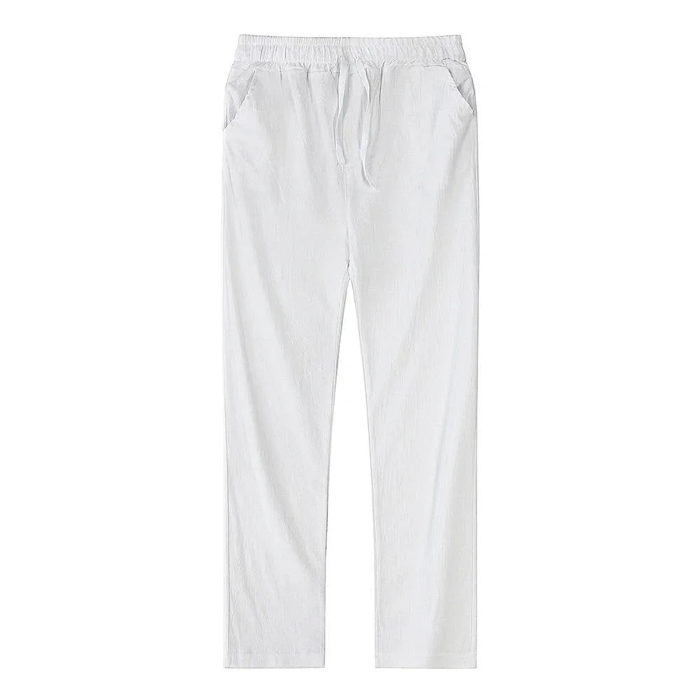 Man wearing light blue linen pants with hand in pocket, viewed from a side angle near the shoreline