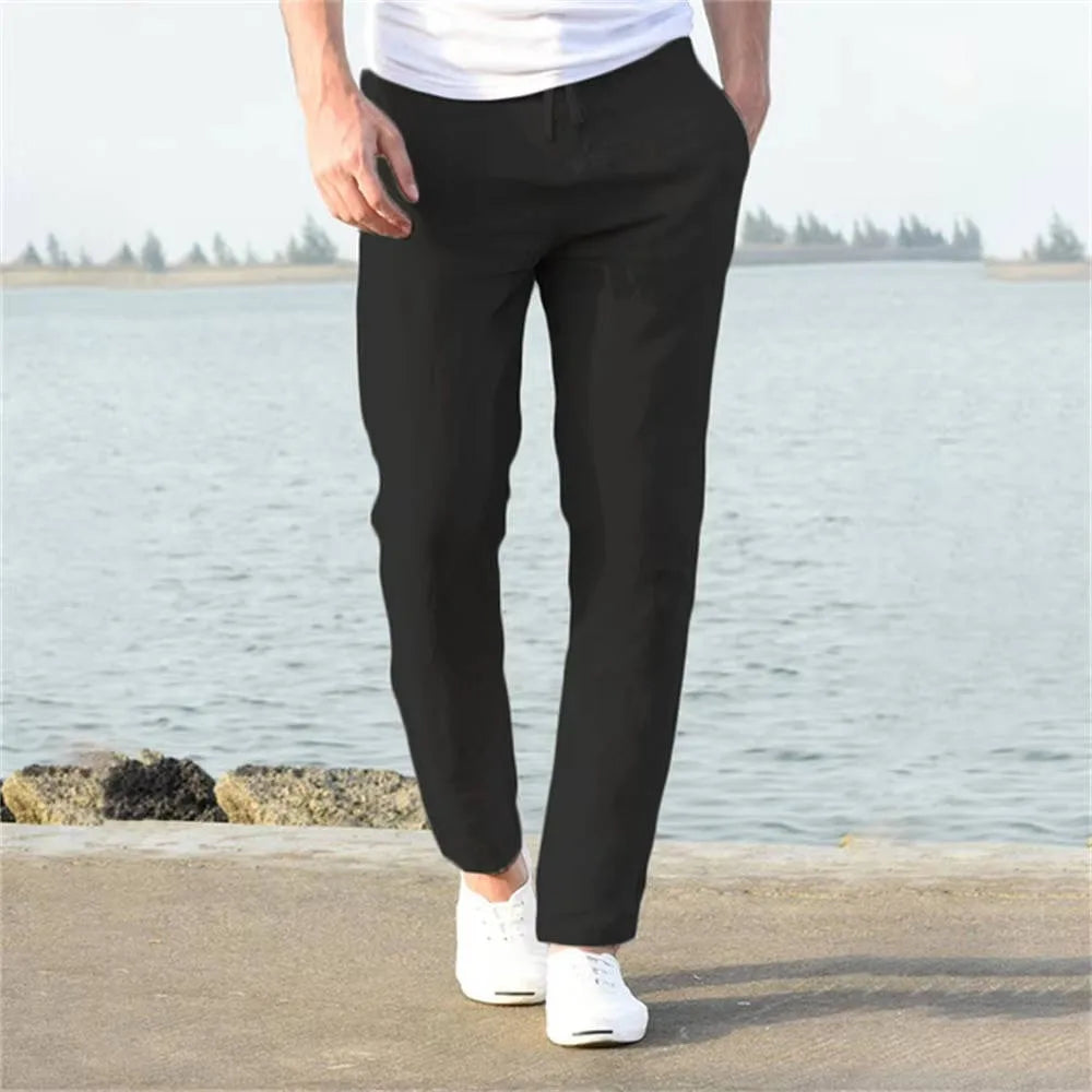 Man wearing black linen pants from behind, paired with white sneakers on a concrete waterside path
