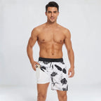 Man in white swim shorts with a black tropical leaf print and black waistband, phone tucked into the side pocket