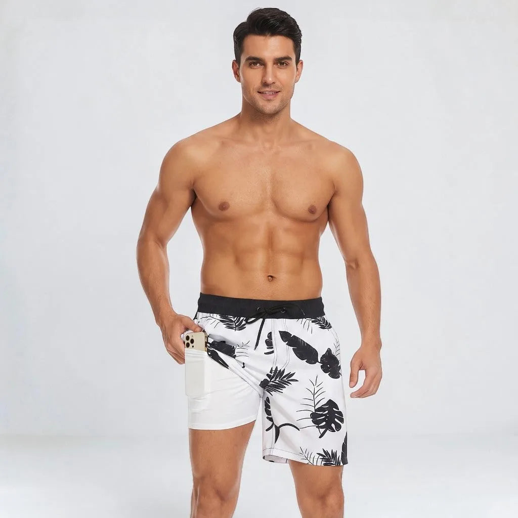 Man in white swim shorts with a black tropical leaf print and black waistband, phone tucked into the side pocket