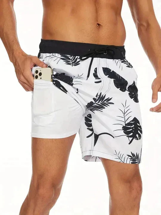Side view of white tropical leaf print swim shorts with black trim, hand holding a phone in the hidden thigh pocket