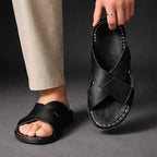 Model wearing black crossover sandals, lifting one shoe to show the contrast topstitching
