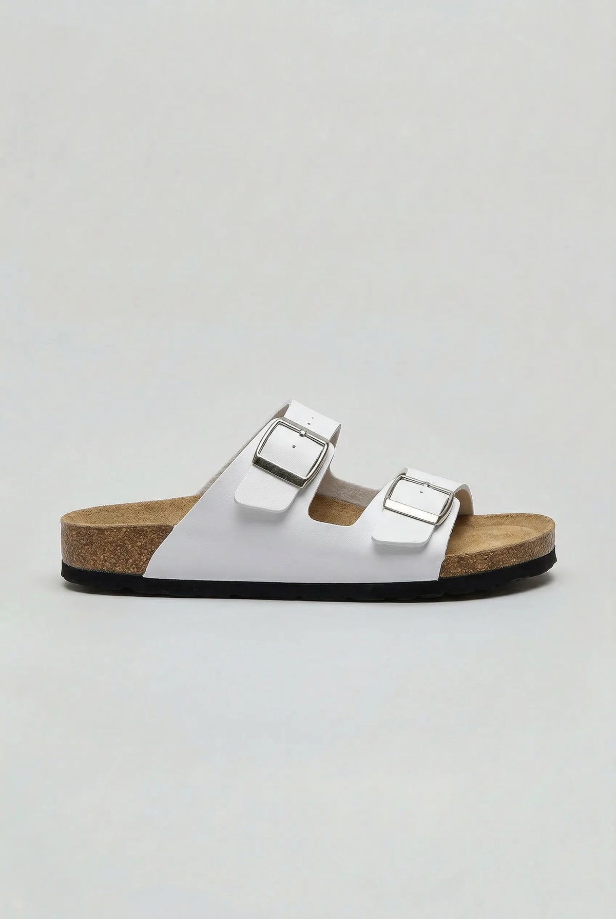 Side profile of a white two-strap buckle sandal with a cork-look footbed and black outsole