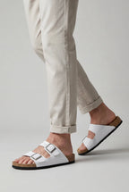 Close-up of a man walking in white double-buckle sandals styled with rolled-up beige trousers