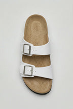 Top-down view of a white two-strap sandal showing the tan footbed and twin metal buckles