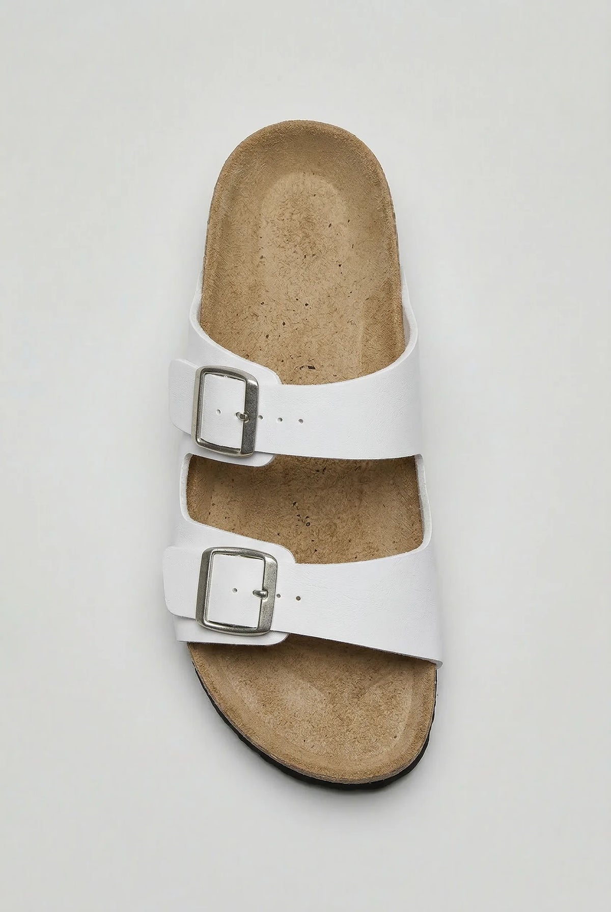 Top-down view of a white two-strap sandal showing the tan footbed and twin metal buckles