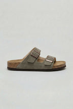 Side view of a dusty green suede two-strap sandal with brown outsole and bronze-tone buckles