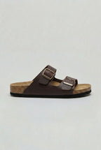 Side view of a dark brown two-strap sandal with bronze buckles and a cork-effect footbed
