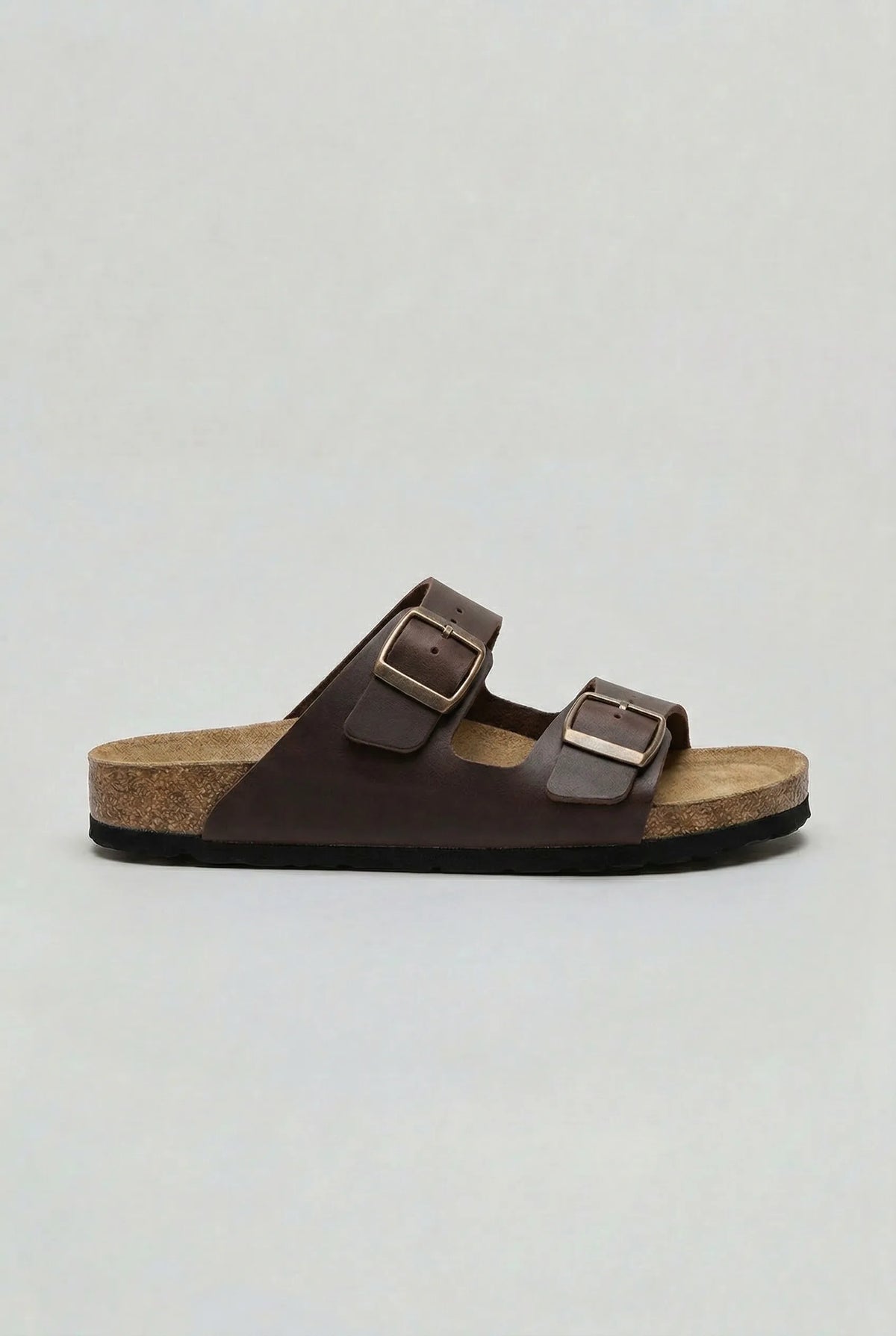 Side view of a dark brown two-strap sandal with bronze buckles and a cork-effect footbed