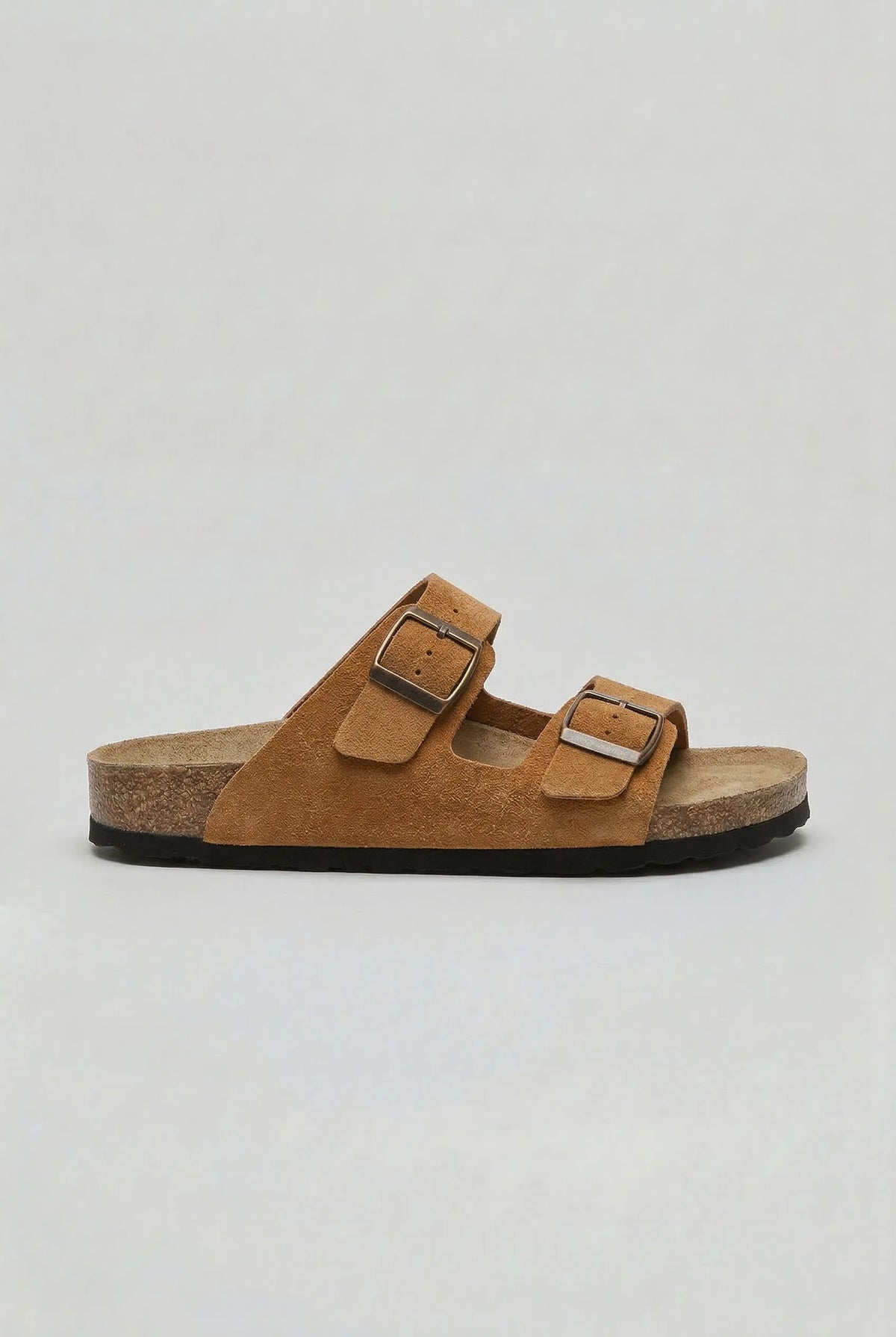 Side view of a rust tan suede two-strap sandal with brown outsole and antique-finish buckles