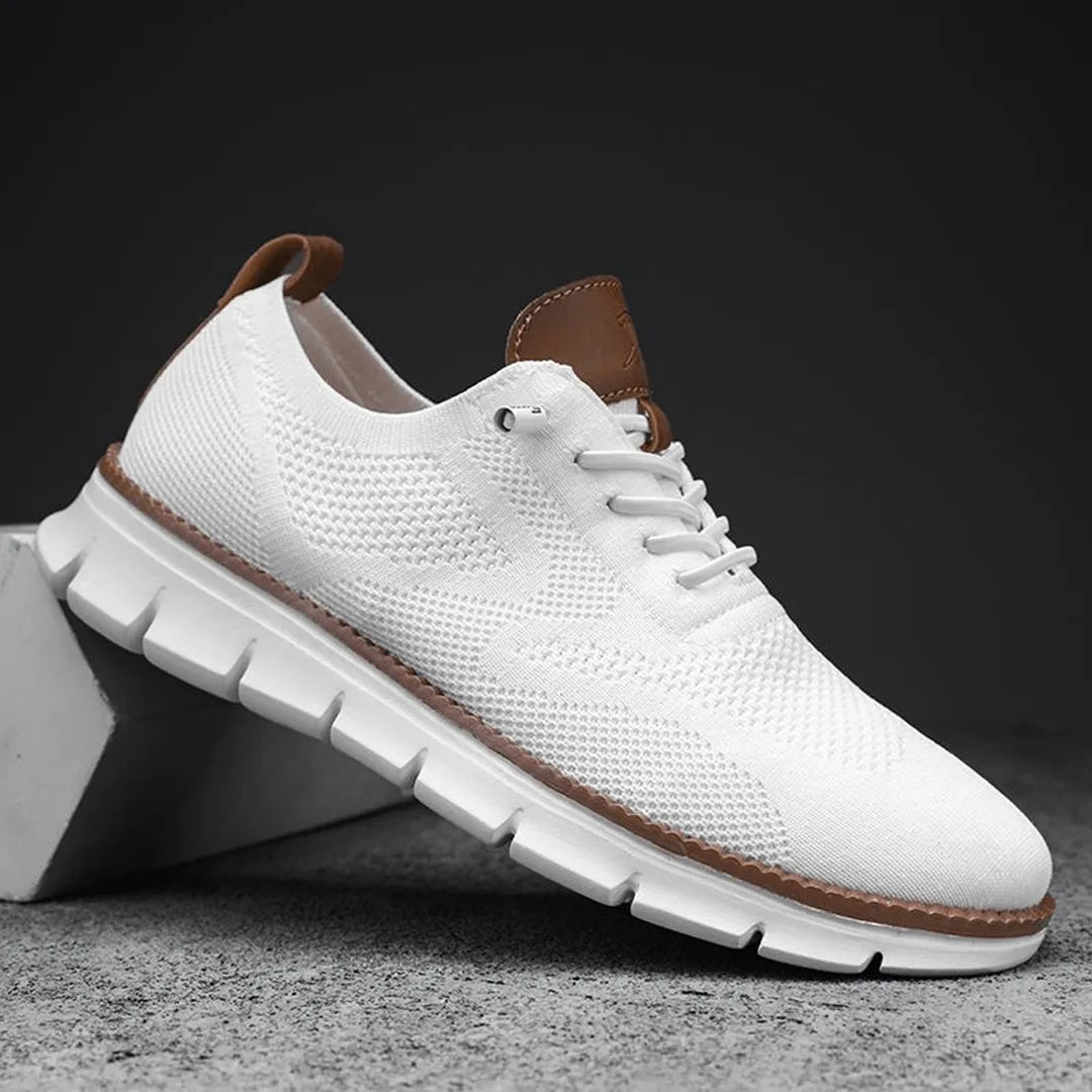 Side profile of white knit sneaker on dark concrete block background, showing tan leather accents