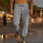 Man walking on wet sand at dusk wearing grey linen-blend drawstring pants with gathered ankle hems