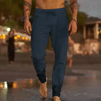 Man walking at dusk on sand wearing navy blue linen-blend drawstring pants with jogger-style cuffs