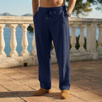 Man wearing navy blue linen drawstring pants with tan loafers on a stone terrace overlooking the sea