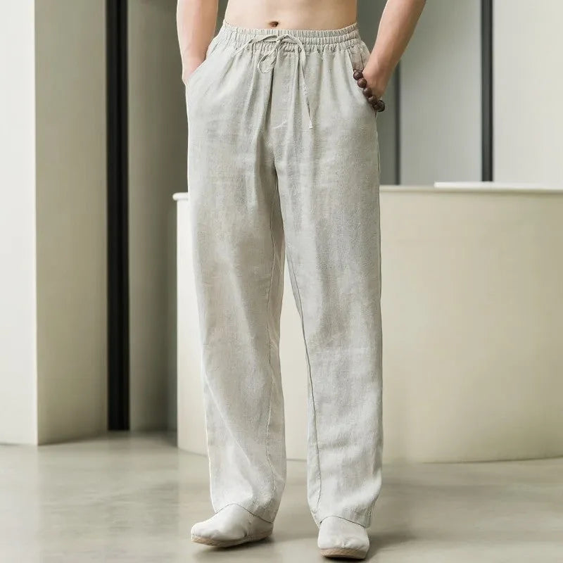 Front view of man wearing pearl grey linen drawstring pants with hands in pockets, elastic waist visible