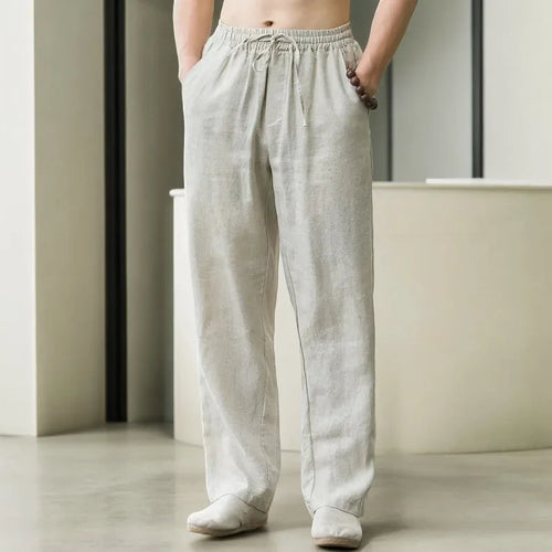 Front view of man wearing pearl grey linen drawstring pants with hands in pockets, elastic waist visible