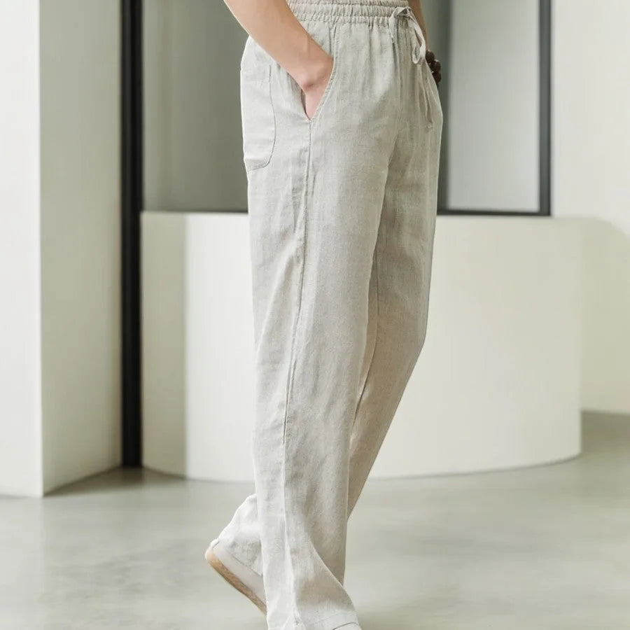 Side profile of pearl grey linen pants showing relaxed straight leg and front pocket detail while walking