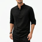 Man wearing a black textured grandad collar shirt with half placket, sleeve rolled to the forearm, paired with dark pants