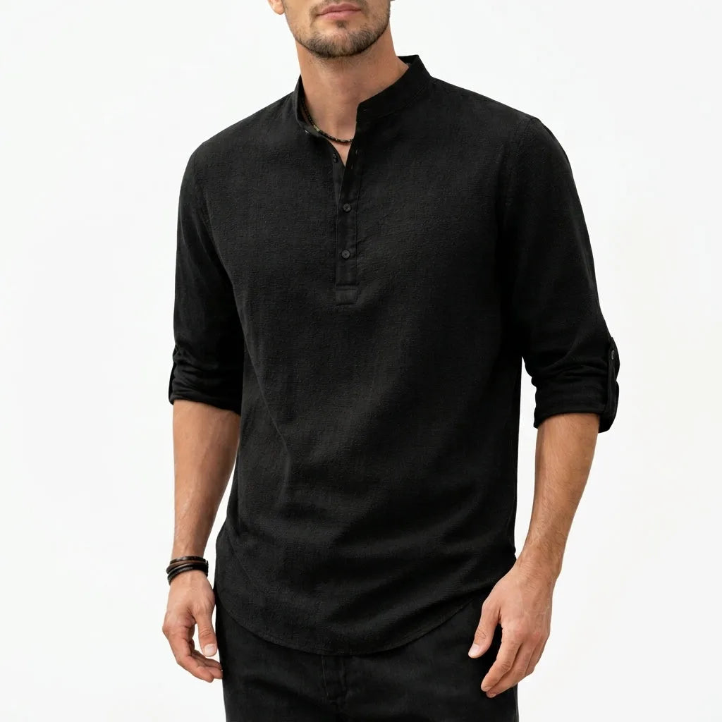 Man wearing a black textured grandad collar shirt with half placket, sleeve rolled to the forearm, paired with dark pants