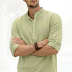 Close-up front view of a sage green grandad collar shirt with half placket buttons and rolled cuffed sleeves, arms crossed