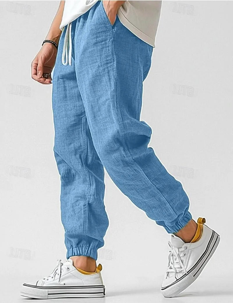 Side profile of man walking in blue linen jogger pants with drawstring waist and elastic cuffs, paired with white sneakers