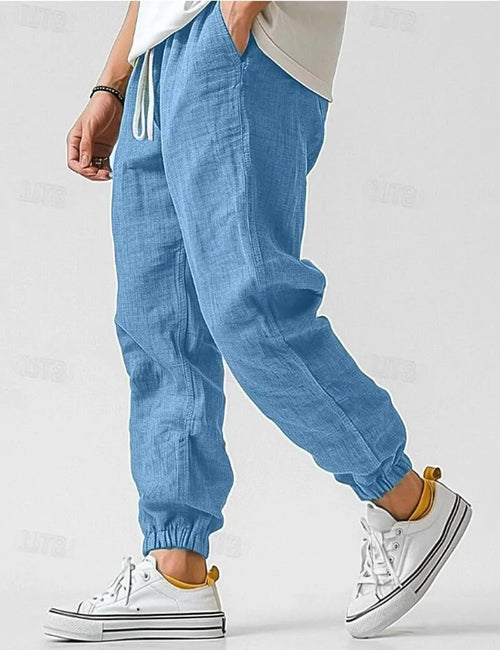 Side profile of man walking in blue linen jogger pants with drawstring waist and elastic cuffs, paired with white sneakers