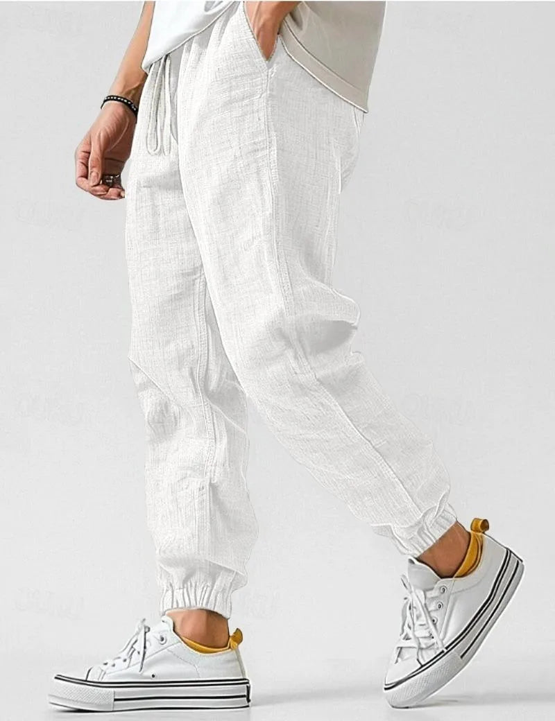Close-up side angle of white linen jogger trousers with elastic cuffed hem and natural woven fabric texture