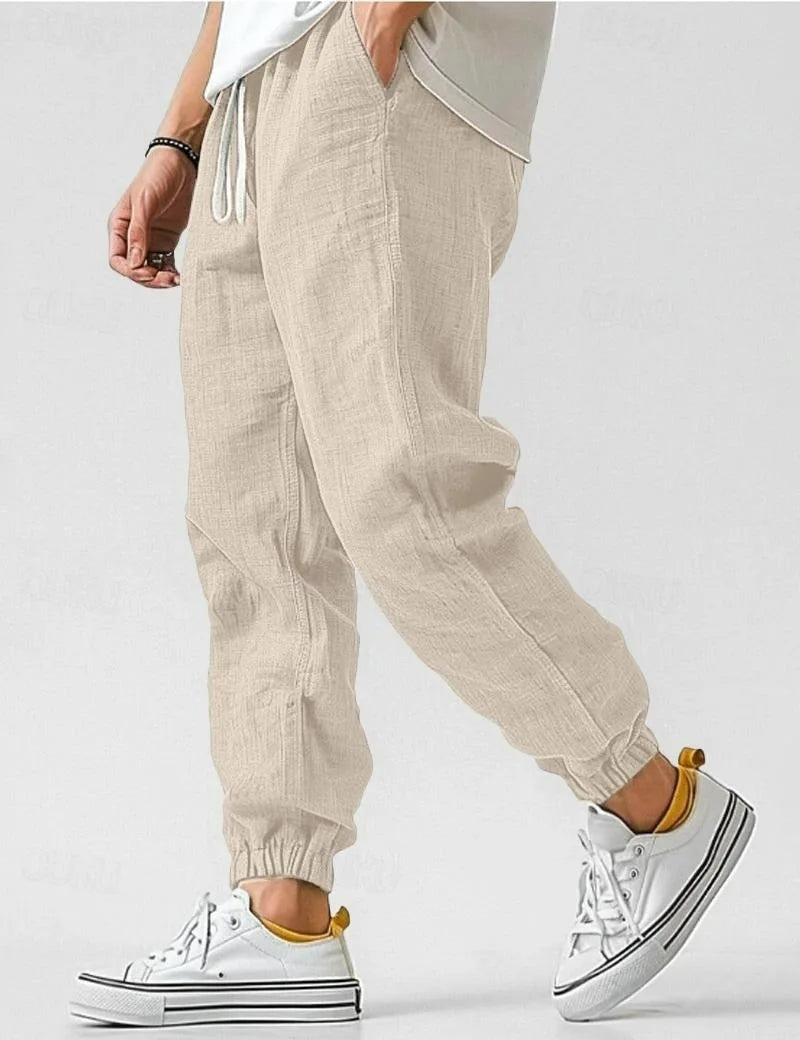 Beige linen jogger pants shown in motion, highlighting the relaxed fit and tapered elastic ankle cuff