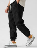 Black linen jogger trousers worn with white sneakers, showing the drawstring waist and side seam detail