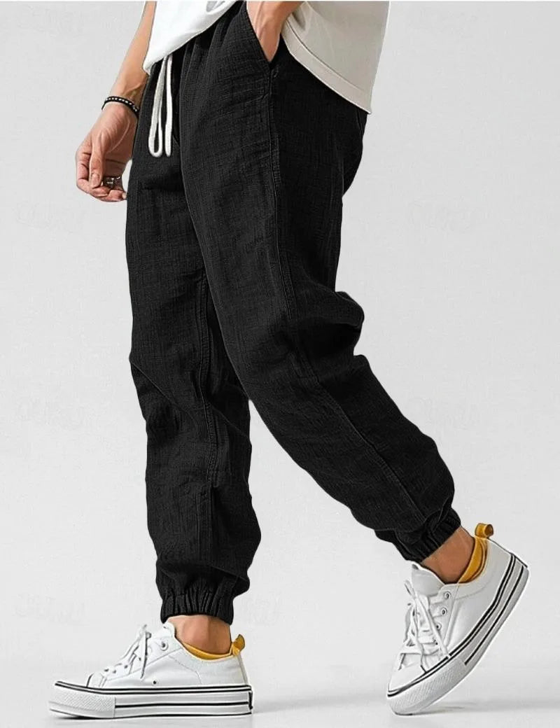 Black linen jogger trousers worn with white sneakers, showing the drawstring waist and side seam detail
