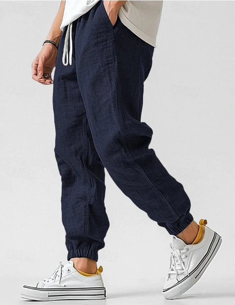 Navy linen jogger pants in profile view, showing the loose tapered leg and elastic cuffed ankle