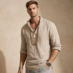 Man wearing a cream linen popover shirt with notched collar, open button placket and rolled sleeves, layered with beaded necklaces.